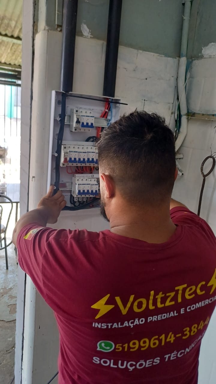 Profissional da VoltzTec, de uniforme, trabalhando em quadro elétrico